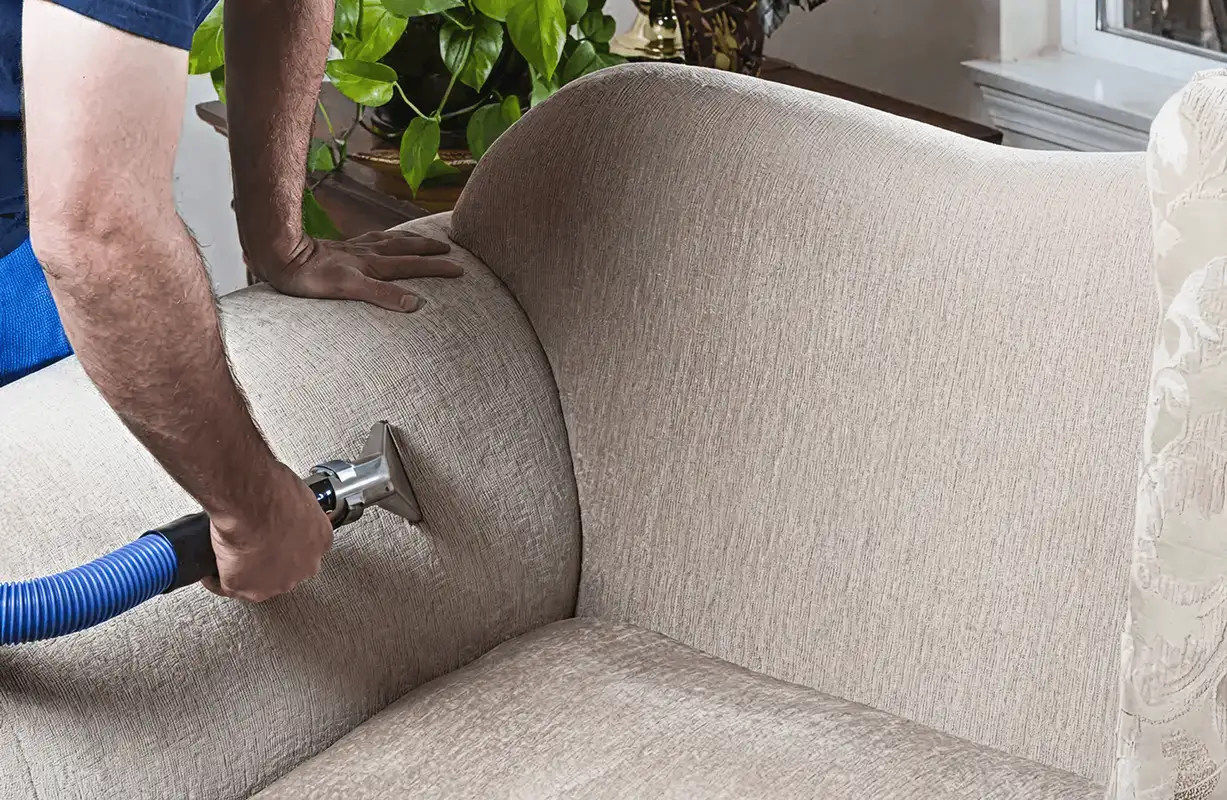 Professional upholstery cleaner deep-cleaning a fabric sofa with a handheld extraction tool and hose, Raleigh, NC.